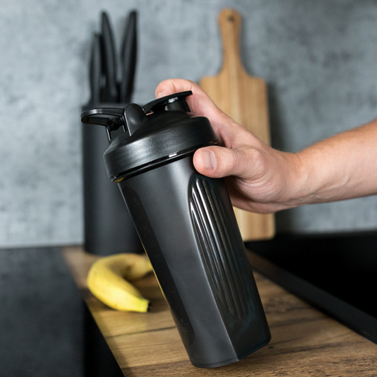 Dłoń trzymająca czarny bidon sportowy z prążkowanym korpusem w nowoczesnej kuchni